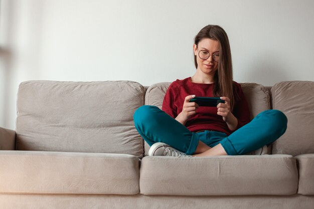 Woman using mobile phone, holding in hands sitting on sofa