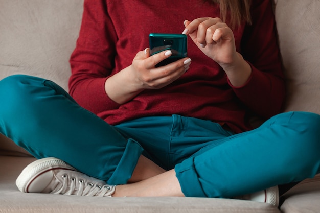 Woman using mobile phone, holding in hands sitting on sofa