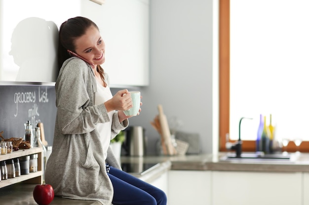 Woman using mobile phone sitting in modern kitchen