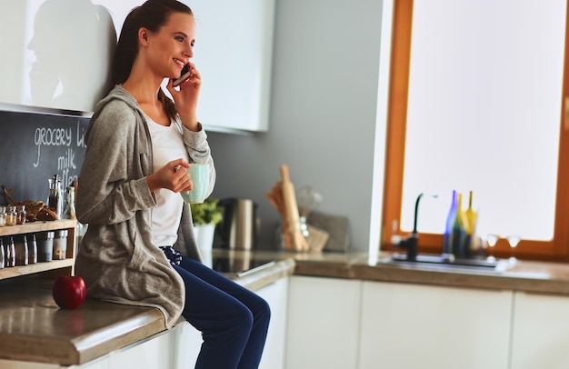 Woman using mobile phone sitting in modern kitchen