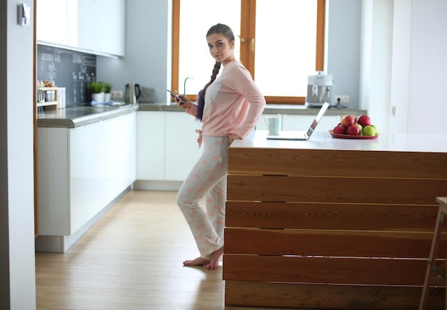 Woman using mobile phone standing in modern kitchen