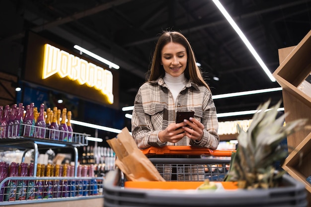 Woman using mobile phone while shopping in supermarket