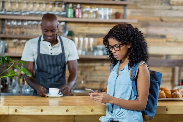 Woman using mobile phone while waiter standing