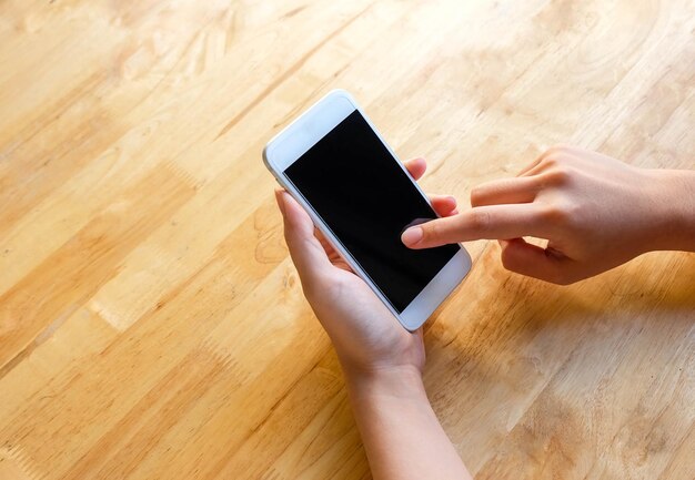 Woman using mobile phone on the wooden table close up