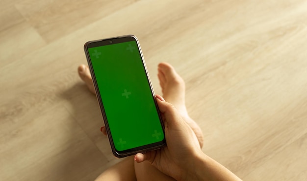 Woman using mobile smart phone with green screen sitting on the floor