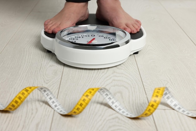 Woman using scales on floor near measuring tape closeup Overweight problem