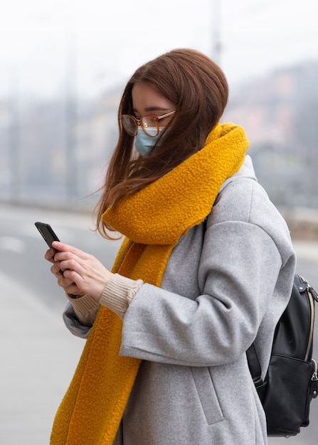 Woman using smartphone in the city while wearing medical mask