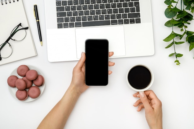 Woman using smartphone and drinking coffee at the office