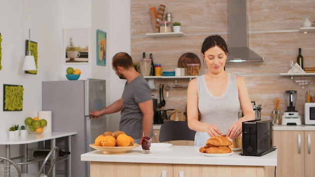 Woman using toaster to roast bread in kitchen during breakfast. Young housewife at home cooking morning meal, cheerful with affection and love