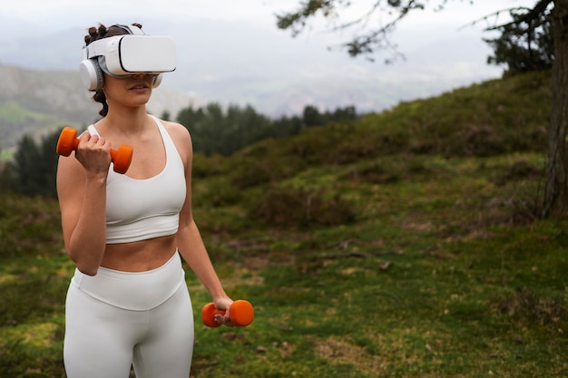 Woman using vr glasses to exercise outdoors with weights