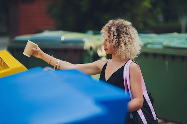 Woman using waste separation container throwing away coffee cup made of Styrofoam