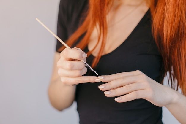 Woman varnishes nail using a thin brush on her fingers.