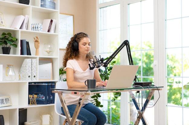 Woman vlogger looking at laptop and recording video with microphone