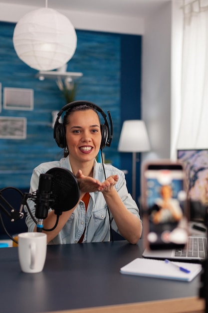 Woman vlogger recording live stream podcast on smartphone. Influencer talking in front of mobile phone camera and filming video for social media channel, using microphone and headphones.