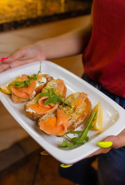 Woman waiter holding a wooden tray with bruschetta in her hand