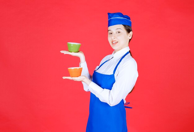 Woman waitress in uniform standing and holding colorful bowls on red wall .