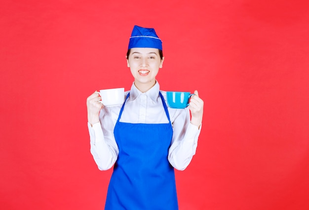 Woman waitress in uniform standing and holding colorful cups on red wall .