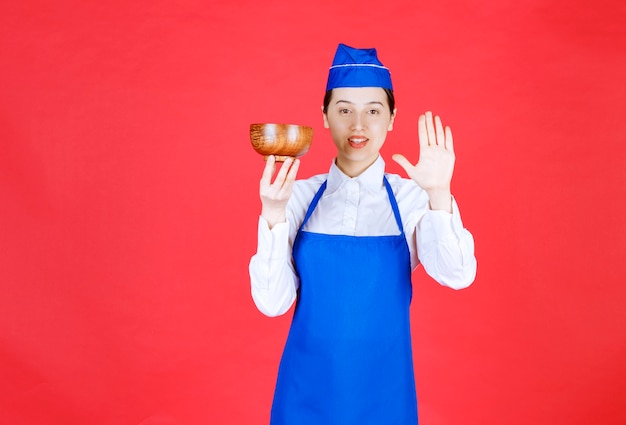 Woman waitress in uniform standing with a wooden bowl and making stop sign .