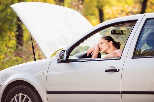 A woman waits for assistance near her car broken down on the road side