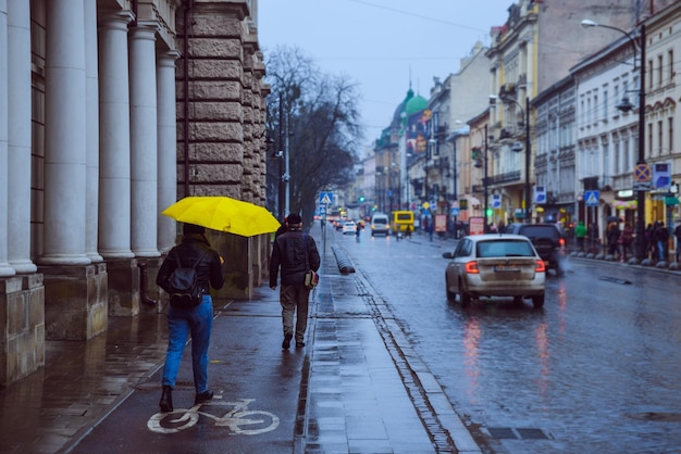 Woman walk by side walk with yellow umbrella rainy weather in old european city