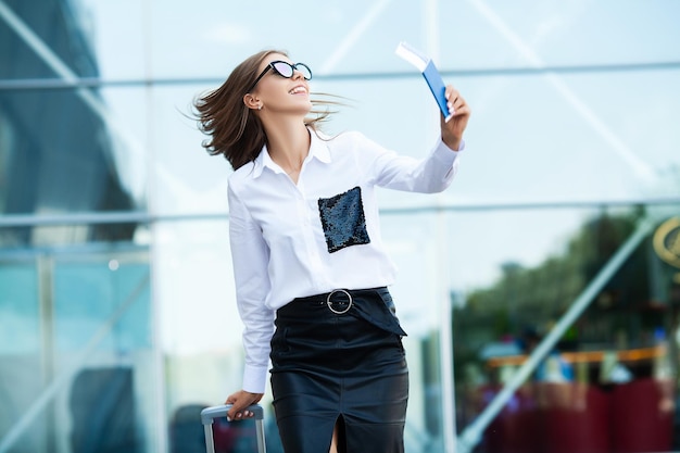 Woman walk near airport with suitcase passport and passenger ticket