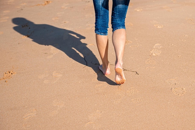 Woman walking barefoot on beach during a sunny day rear view closeup