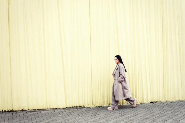 Woman walking in a beige coat against urban city background