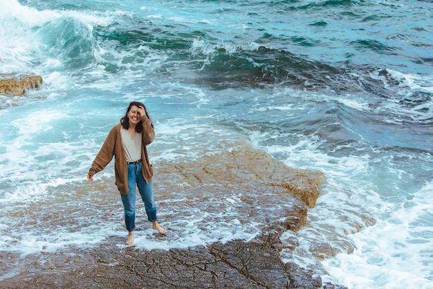 Woman walking by rocky beach in wet jeans barefoot summer sea vacation