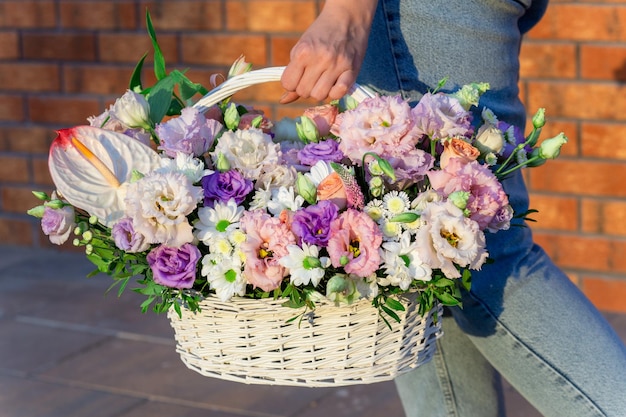 Woman walking and holding big and beautiful wicker basket with fresh roses eustoma and other flowers