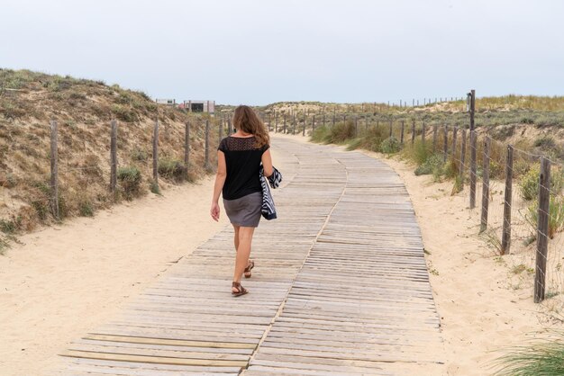 Photo woman walking on the sandy beach rear view in path wooden