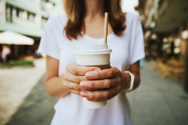 Woman walks at city street and drinks coffee to go