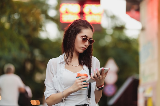 Woman walks down the street with coffee and phone in her hands. High quality photo