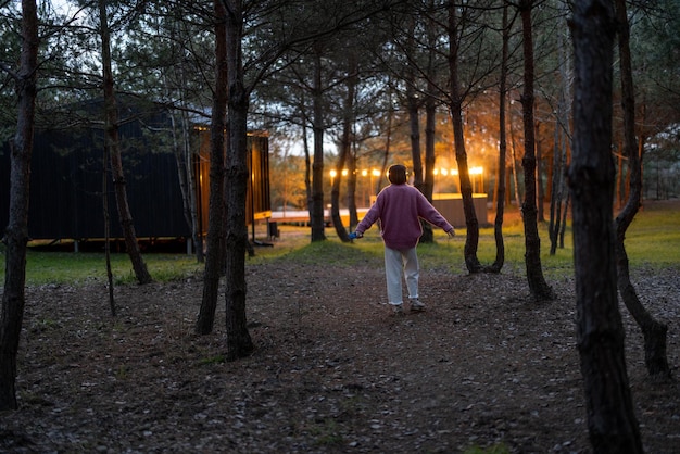 Woman walks in pine forest near wooden cottage at dusk