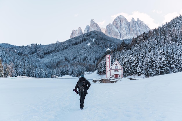 Woman walks through the snow to church in the middle of the alps with snow-capped mountains in the background