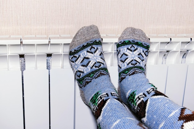 A woman warms her frozen feet in socks on a battery The concept of heat in the house Cold season