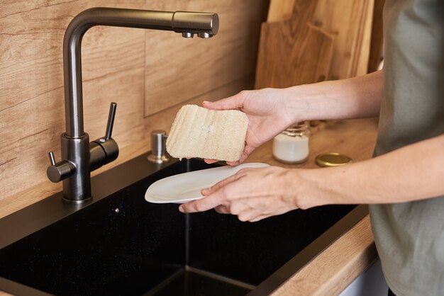 Woman washes dishes with organic eco friendly sponge. Zero waste concept