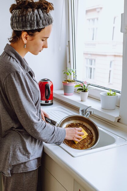 A woman washing dishes in a kitchen with a sponge in her hand.