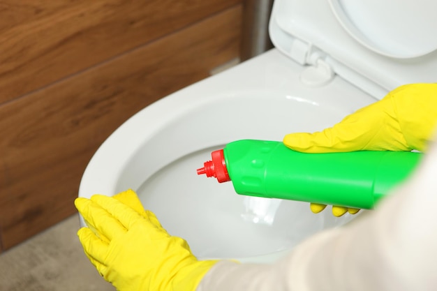 Woman washing and disinfecting toilet bowl with detergent closeup