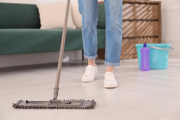 Woman washing floor with mop in living room closeup