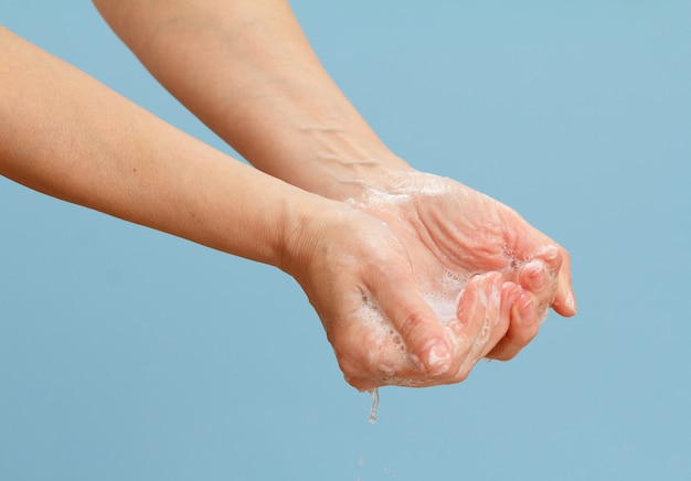 Woman washing hands with soap on a blue surface