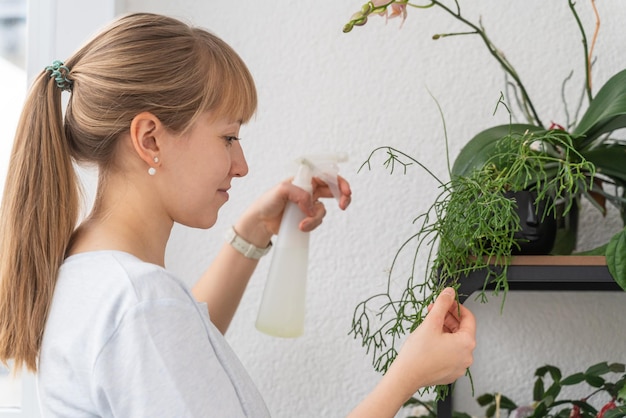 Woman watering plants and flowers with plastic bottle on balcony. Botanical hobby