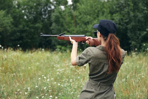 Woman Weapon aiming hunting back view on outdoor green overalls