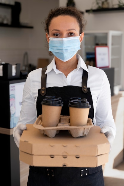 Woman wearing apron and holding packed takeaway food and coffee cups