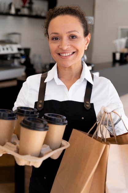 Woman wearing apron and holding paper bags with takeaway food and coffee cups