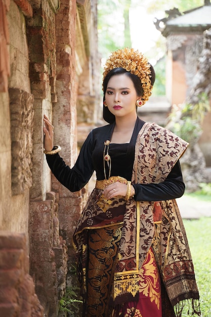 Woman wearing balinese kebaya standing next to a relief wall