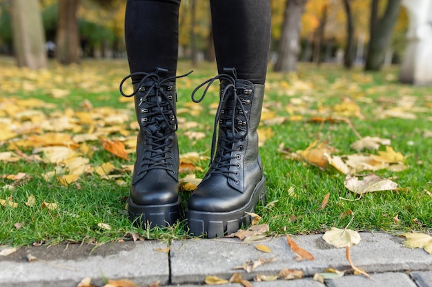 A woman wearing black boots stands in the grass in autumn.