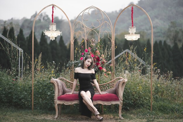 Photo woman wearing black dress sitting on the couch on flowers garden.