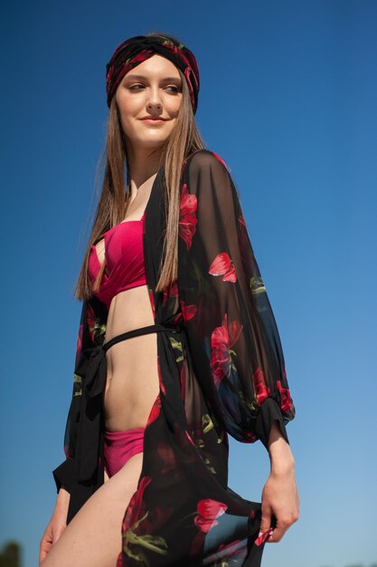 A woman wearing a black kimono and a red hat stands in front of a blue sky.