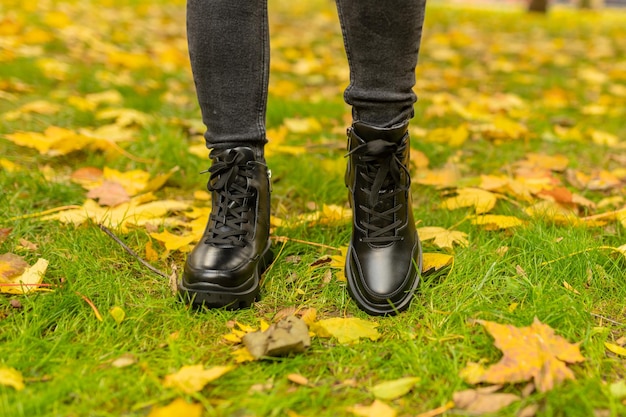 A woman wearing black leather shoes stands on the grass in autumn.