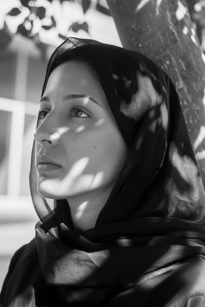 Photo a woman wearing a black scarf is standing in front of a tree